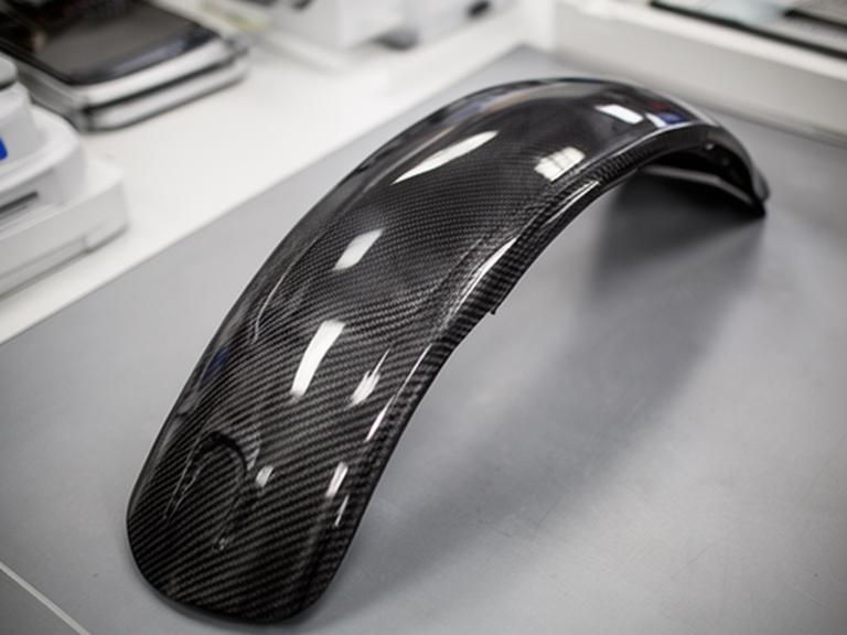 Fender de carbono con trama visible en una mesa de inspección técnica