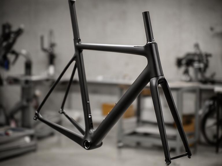 Cuadro de bicicleta de fibra de carbono colgado en taller con acabado mate uniforme